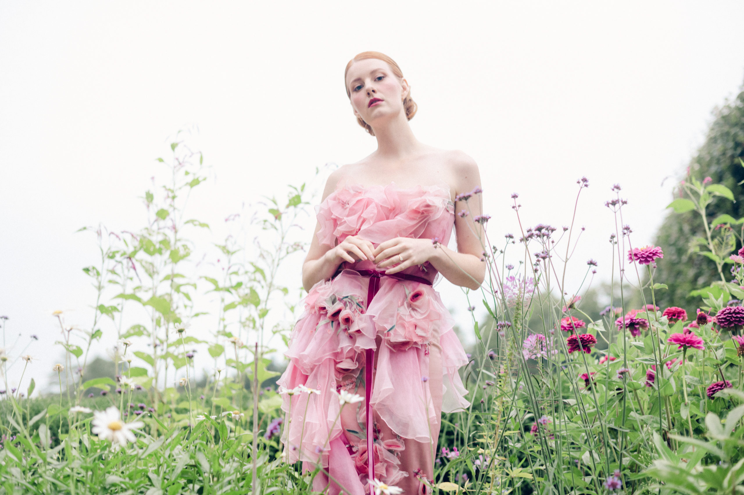 Model standing in a garden of flowers wearing a rare pink Marchesa gown.